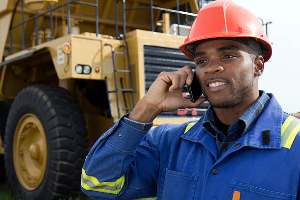 A royalty free image from the mining industry of a miner using a cellphone in front of a dump truck.
